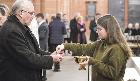 Bischof Rudolf Voderholzer empfängt die heilige Kommunion von einer jungen Frau.